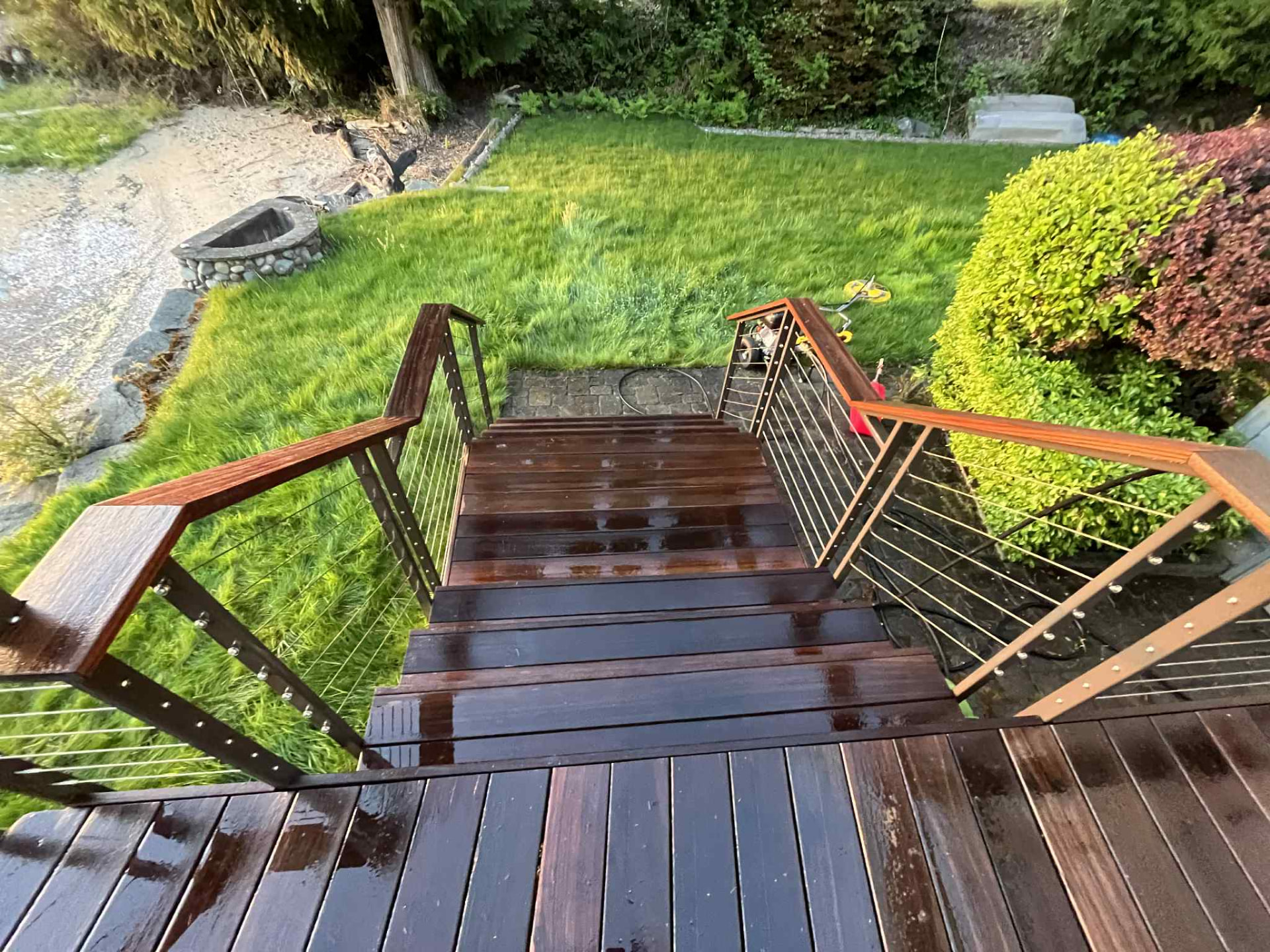 Freshly oiled deck steps with cable railings looking down over a garden