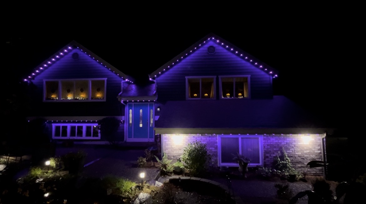 A two-storey house at night with purple permanent lights outlining both gables and warm white lights under the eaves